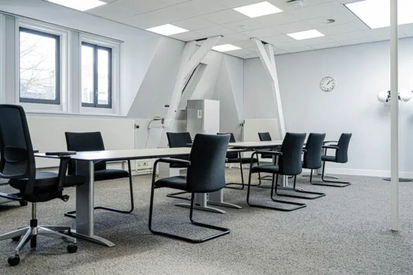 Vergaderruimte aan de Burgemeester van Karnebeeklaan met moderne inrichting en zwart-witte stoelen rond een lange tafel.